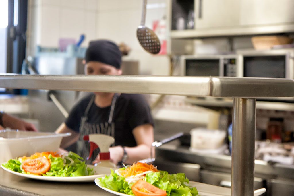 Un plan de travail de cuisine avec deux assiettes de salade, un chef cuisinier en arrière-plan et des appareils de cuisine.