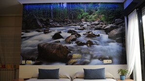 A bedroom with two beds, a mural of a forest stream, and a potted plant. - Hotel Aitana (Irun)