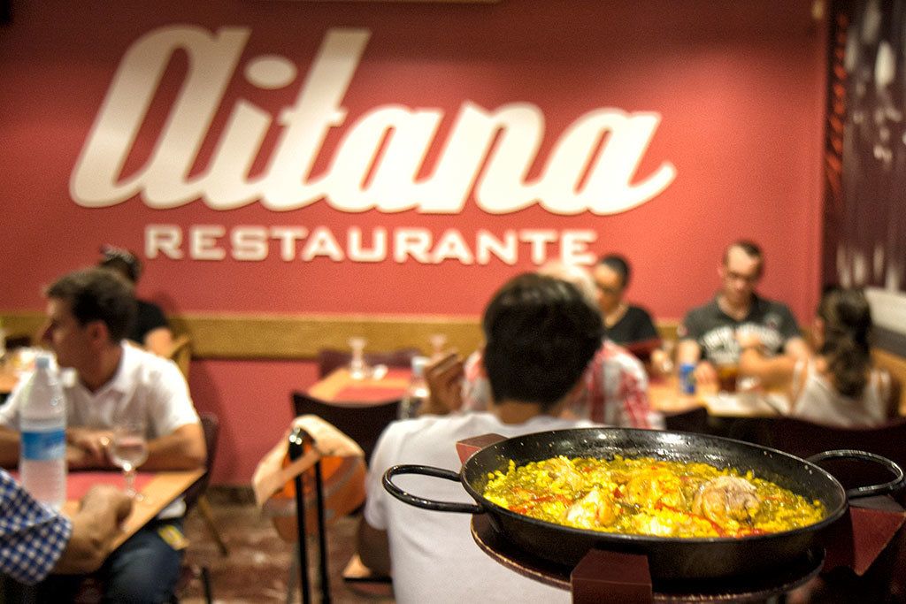 A restaurant named 'Alitana Restaurante' with patrons dining and a large pan of food on the table.