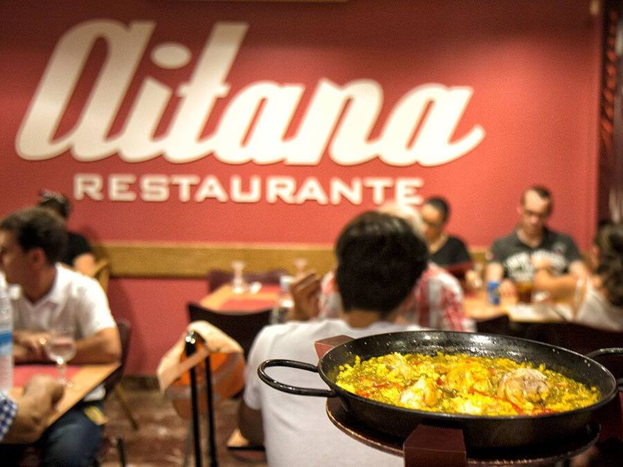 A restaurant named 'Alitana Restaurante' with patrons dining and a large pan of food on the table.