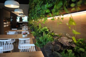 A restaurant interior with wooden tables and chairs, a green wall with plants, and hanging lights. - Hotel Aitana (Irun)