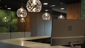 A reception desk with a desktop computer, hanging crystal chandeliers, and a wall with a green leafy pattern. - Hotel Aitana (Irun)