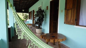 Un porche cubierto con una hamaca, una mesa de madera y una planta en maceta.