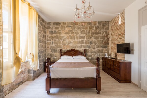 A bedroom with a stone wall, a wooden bed, a dresser, and a television on the wall. - PIETRA ROSSA Luxury Rooms (Split)