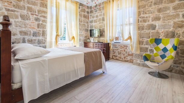 Un dormitorio con pared de piedra, cama, cómoda, televisor y silla.