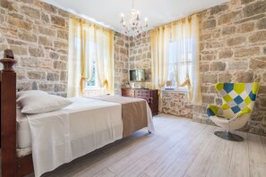 A bedroom with a stone wall, a bed, a dresser, a TV, and a chair. - PIETRA ROSSA Luxury Rooms (Split)