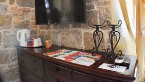 Habitación con pared de piedra, un televisor de pantalla plana sobre una encimera de madera, una cafetera, una revista, el símbolo de Wi-Fi y un teléfono.