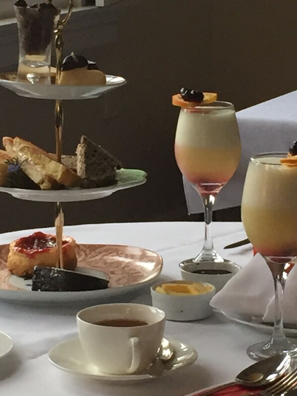 Un elegante expositor de tres niveles con pasteles y un vaso de postre. También hay una taza de café y una cuchara sobre la mesa.