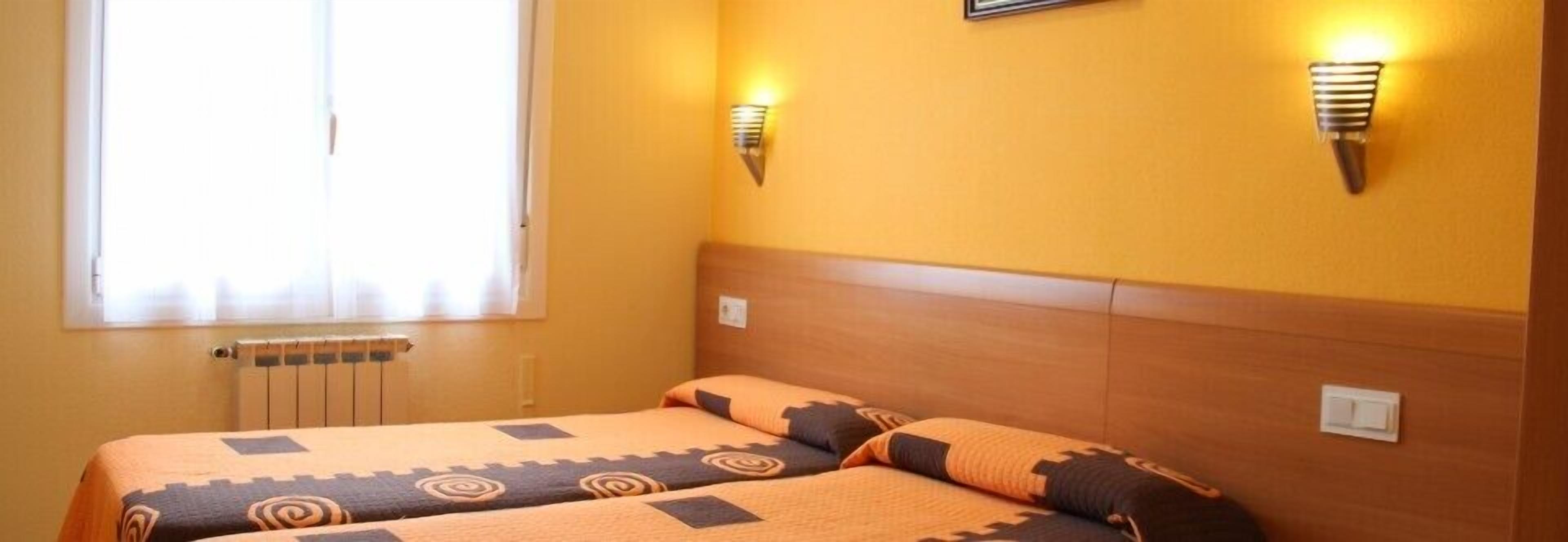 Une chambre d’hôtel avec deux lits, une fenêtre avec des rideaux et des lampes fixées au mur.