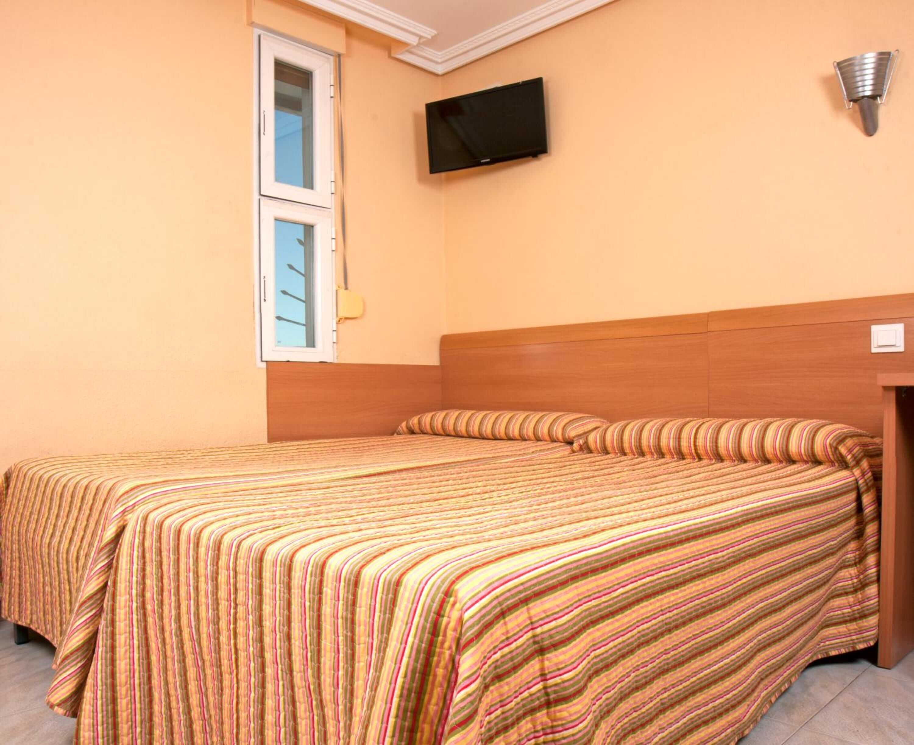 Una cama doble con ropa de cama a rayas, un televisor montado y una ventana con persianas.