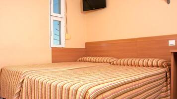 Una cama doble con ropa de cama a rayas, un televisor montado y una ventana con persianas.