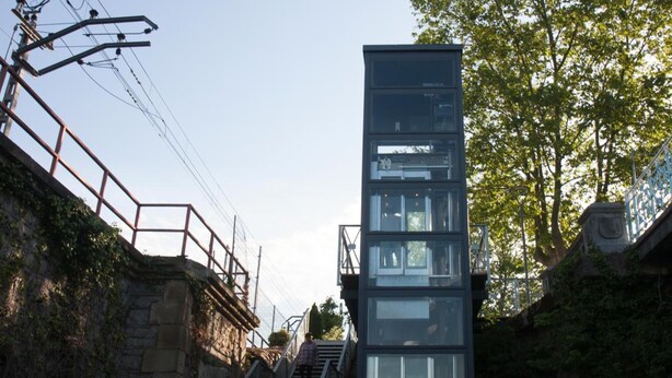 A modern building with a glass facade, a wooden deck, and a metal staircase leading to an entrance. - HOSTAL EUROPA pensión (Irun)