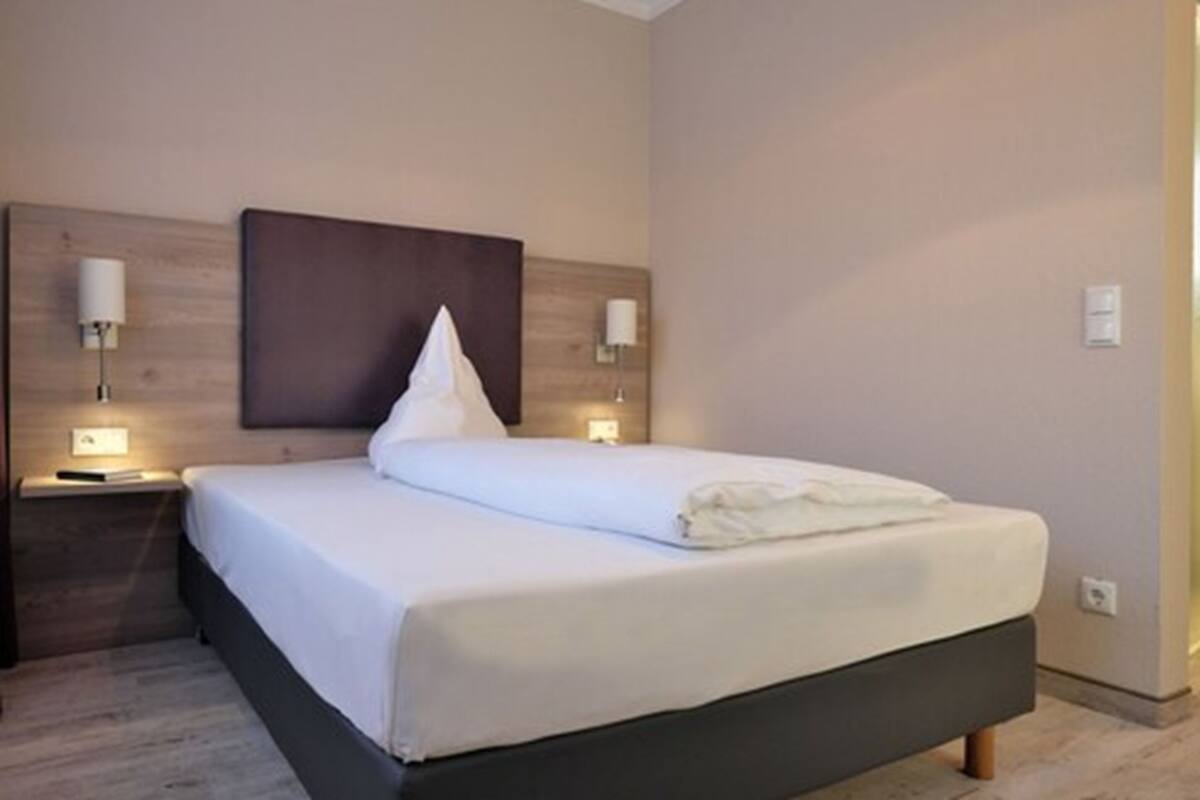 A neatly made bed with a dark headboard, two bedside lamps, and a wooden nightstand.