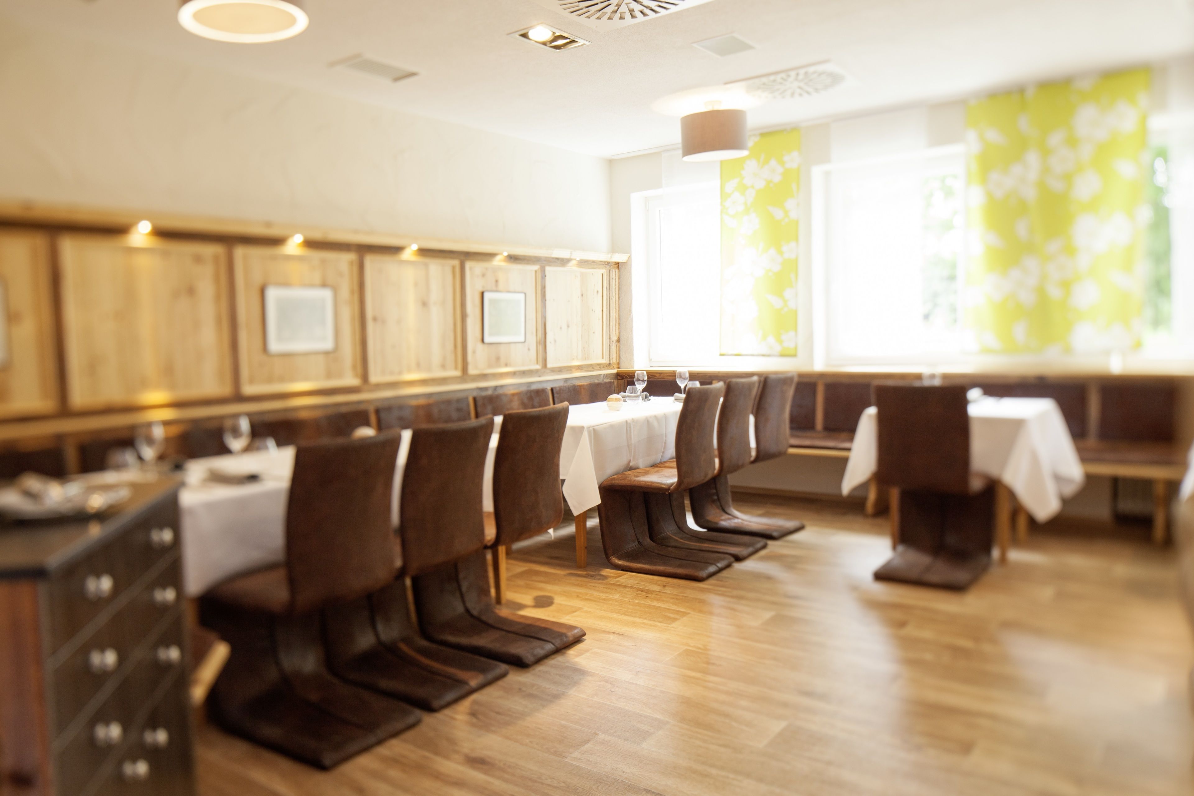 Un restaurant avec des murs lambrés, des tables blanches et des chaises marron.