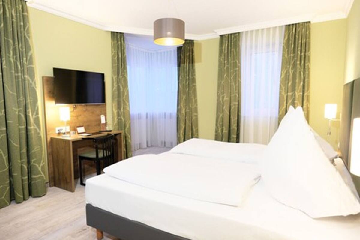 A hotel room with a bed, a desk, a chair, a TV, and curtains.