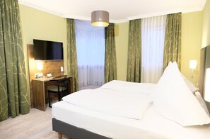 A hotel room with a bed, a desk, a chair, a TV, and curtains. - Hotel Römerstadt (Gersthofen)
