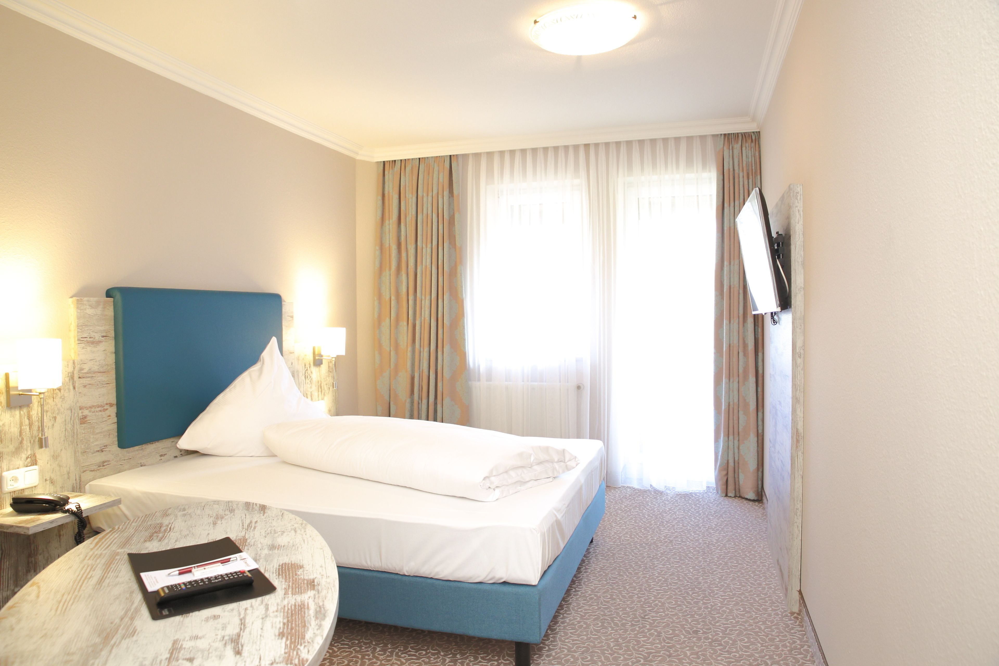 A hotel room with a bed, a small table, a TV, and curtains.