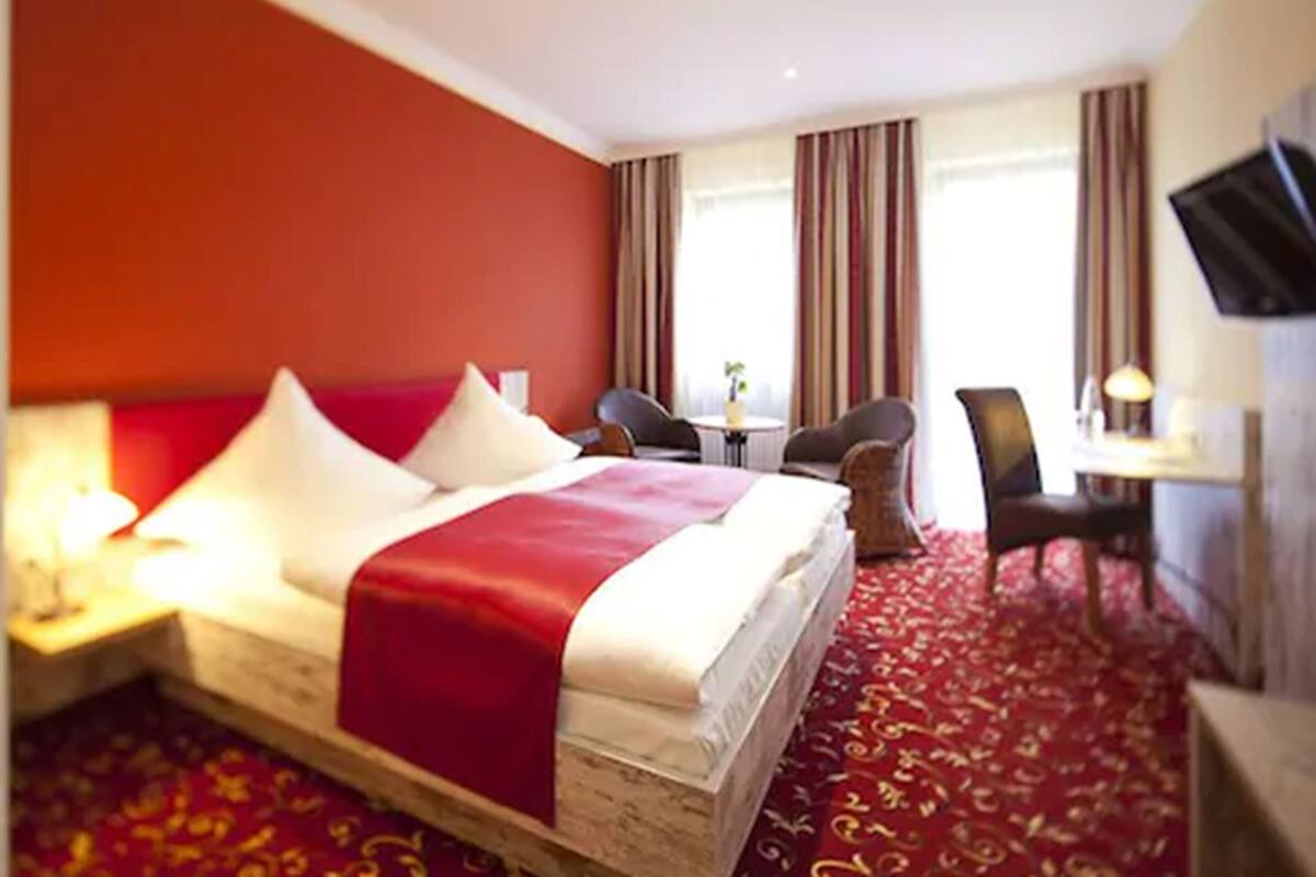 A hotel room with a large bed, a desk with a chair, a TV, and a window with curtains.