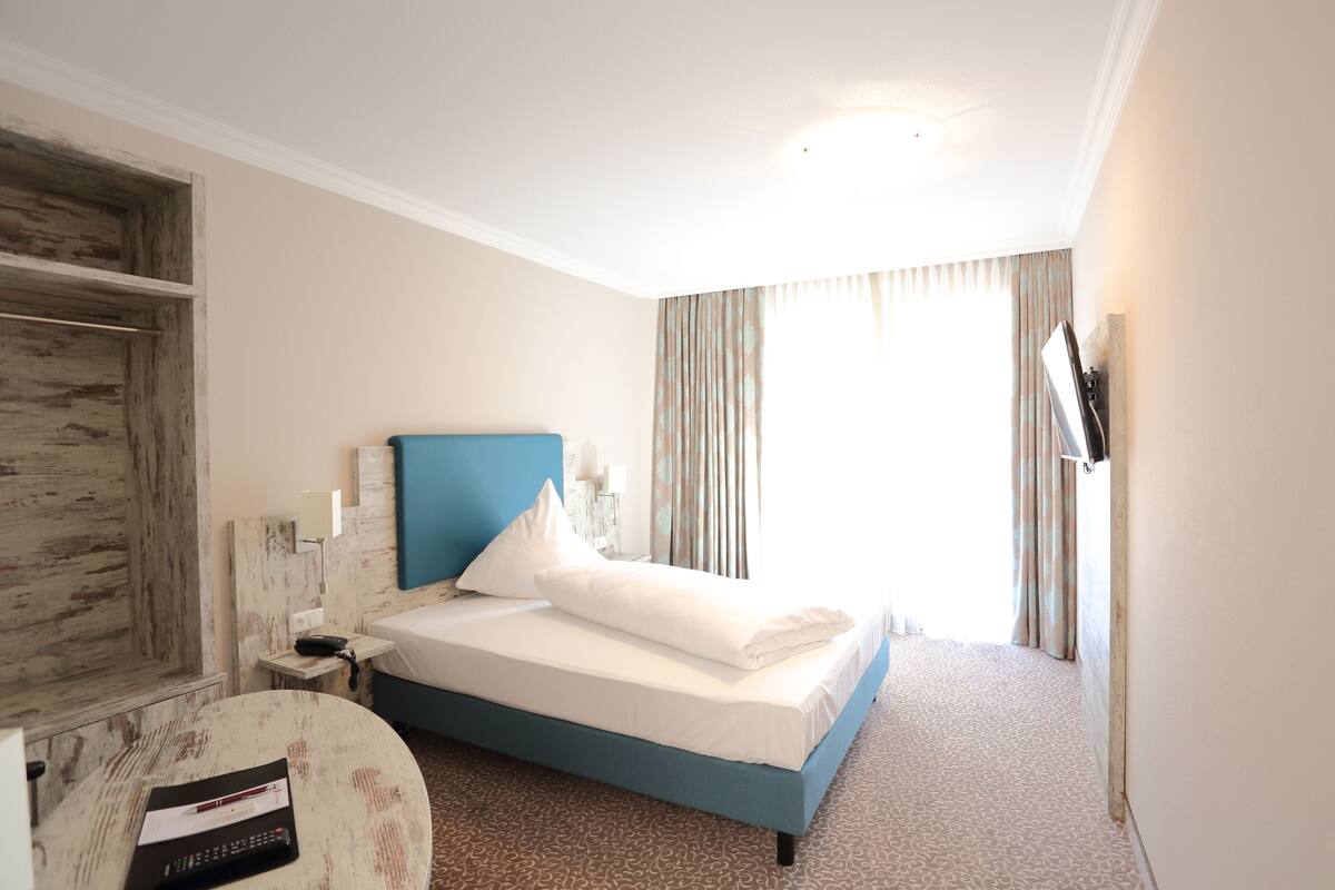 A hotel room with a bed, a desk, a chair, a wardrobe, and a TV.