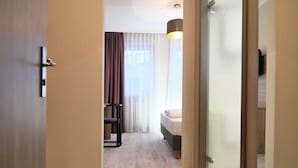 Una habitació d'hotel amb un llit, escriptori, cadira i finestra amb cortines.