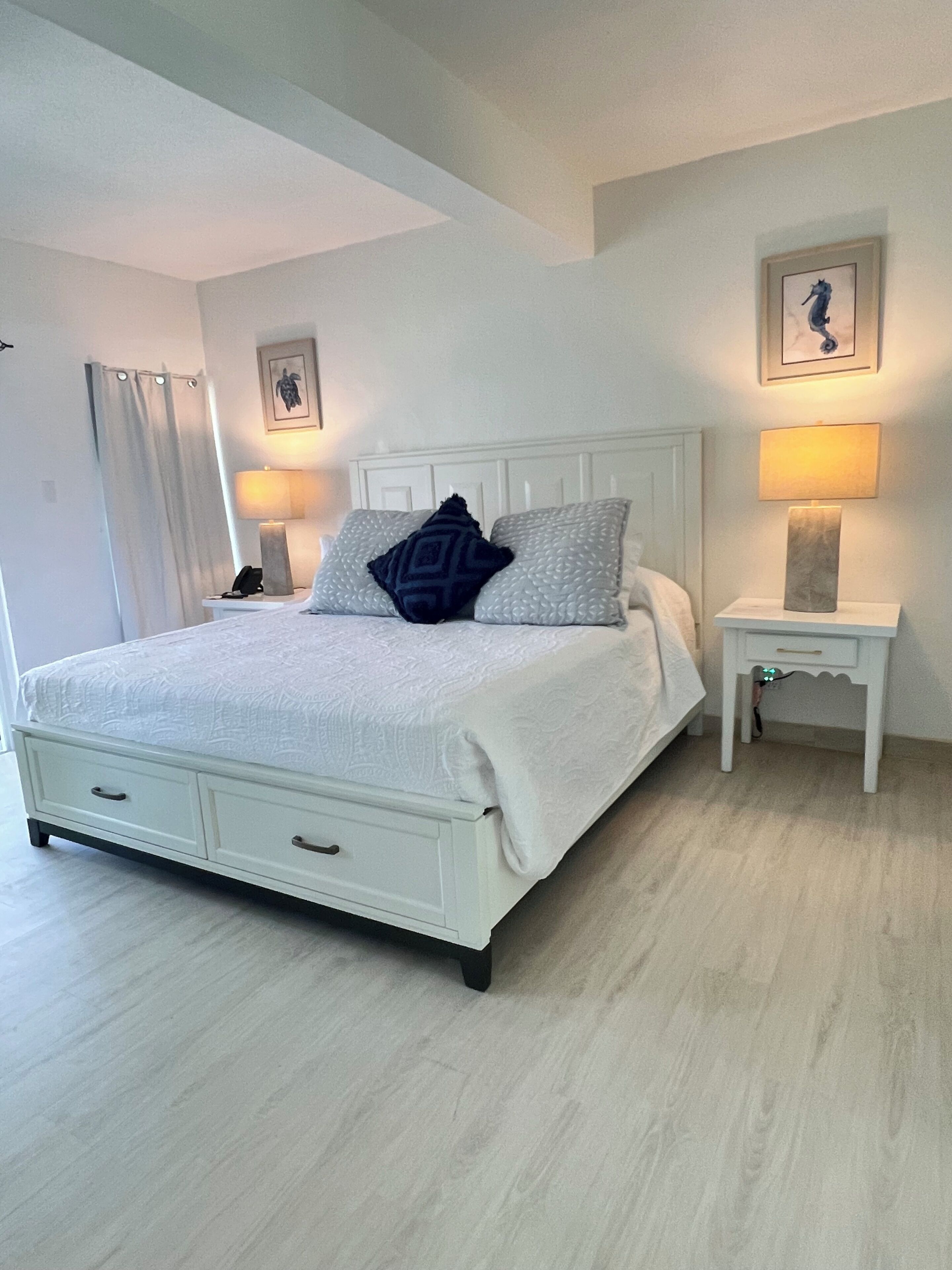 A bedroom with a bed, bedside tables, a lamp, a phone, a picture frame, and a curtain.