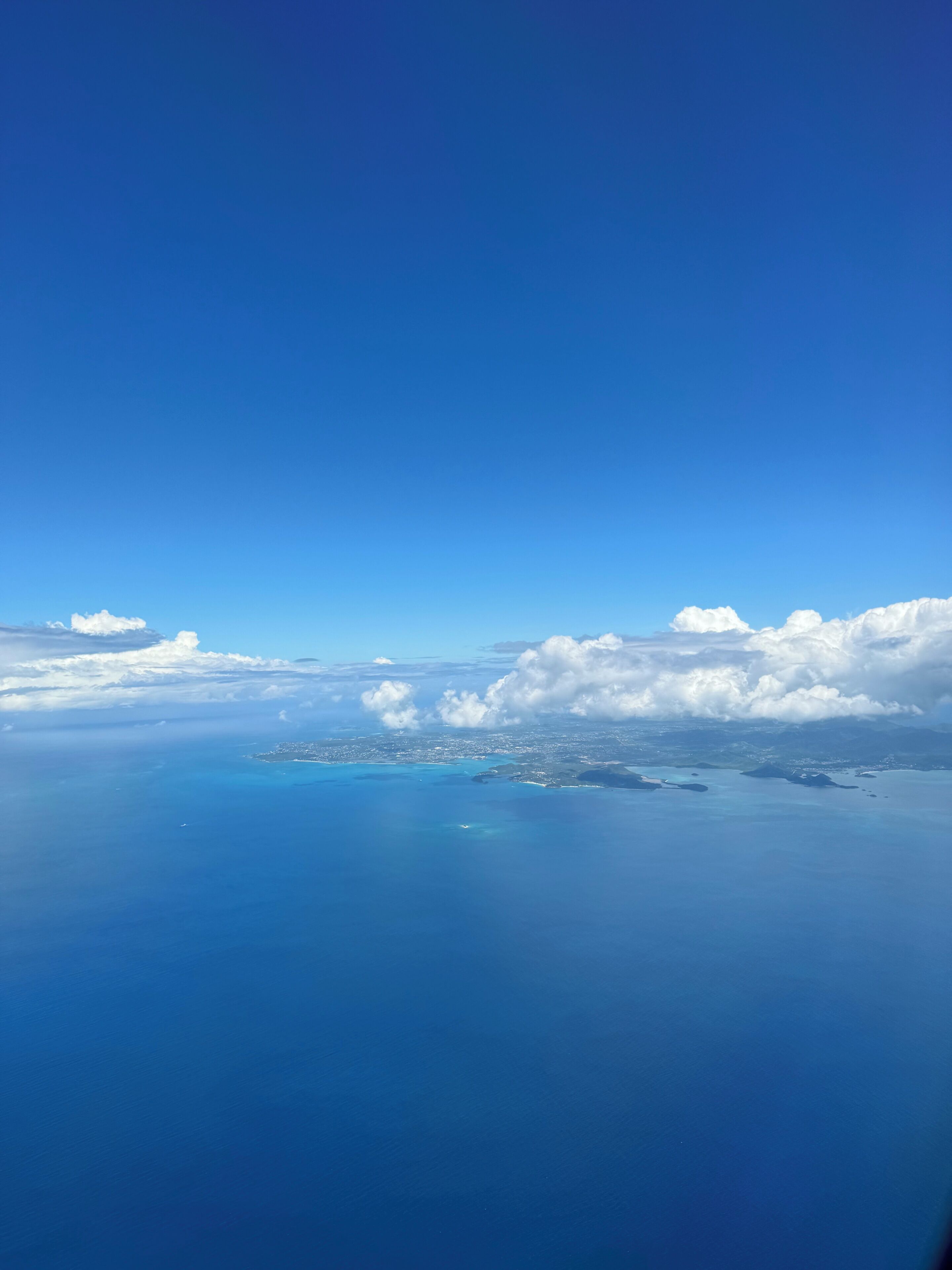 Ein klarer, blauer Himmel mit Wolken und Blick auf eine Küstenlinie.