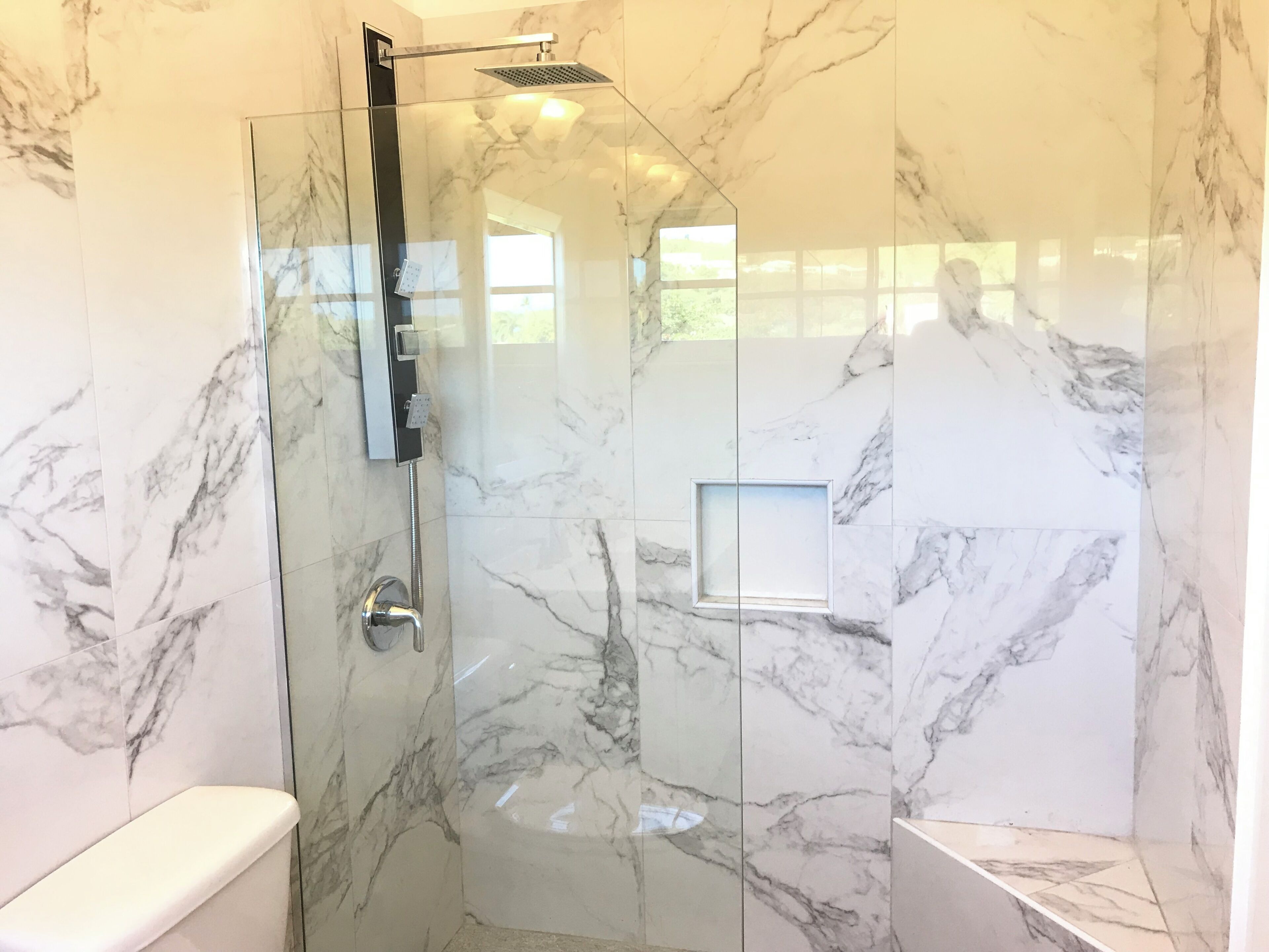 Een moderne badkamer met een douche met glazen wanden, marmeren wanden en een inbouwtoilet.