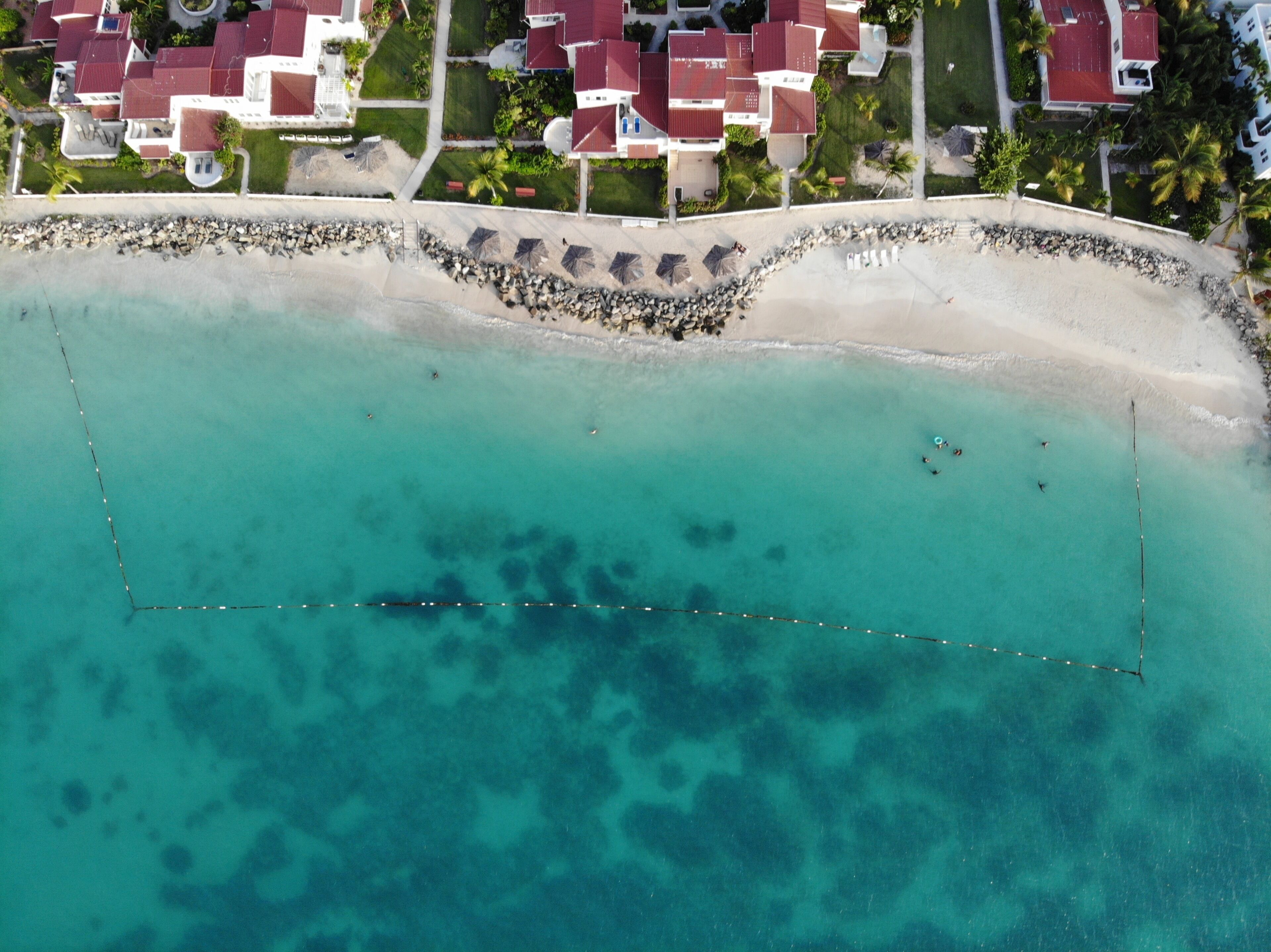 An aerial view of a coastal resort with beachfront properties, a sandy beach, and clear turquoise waters.