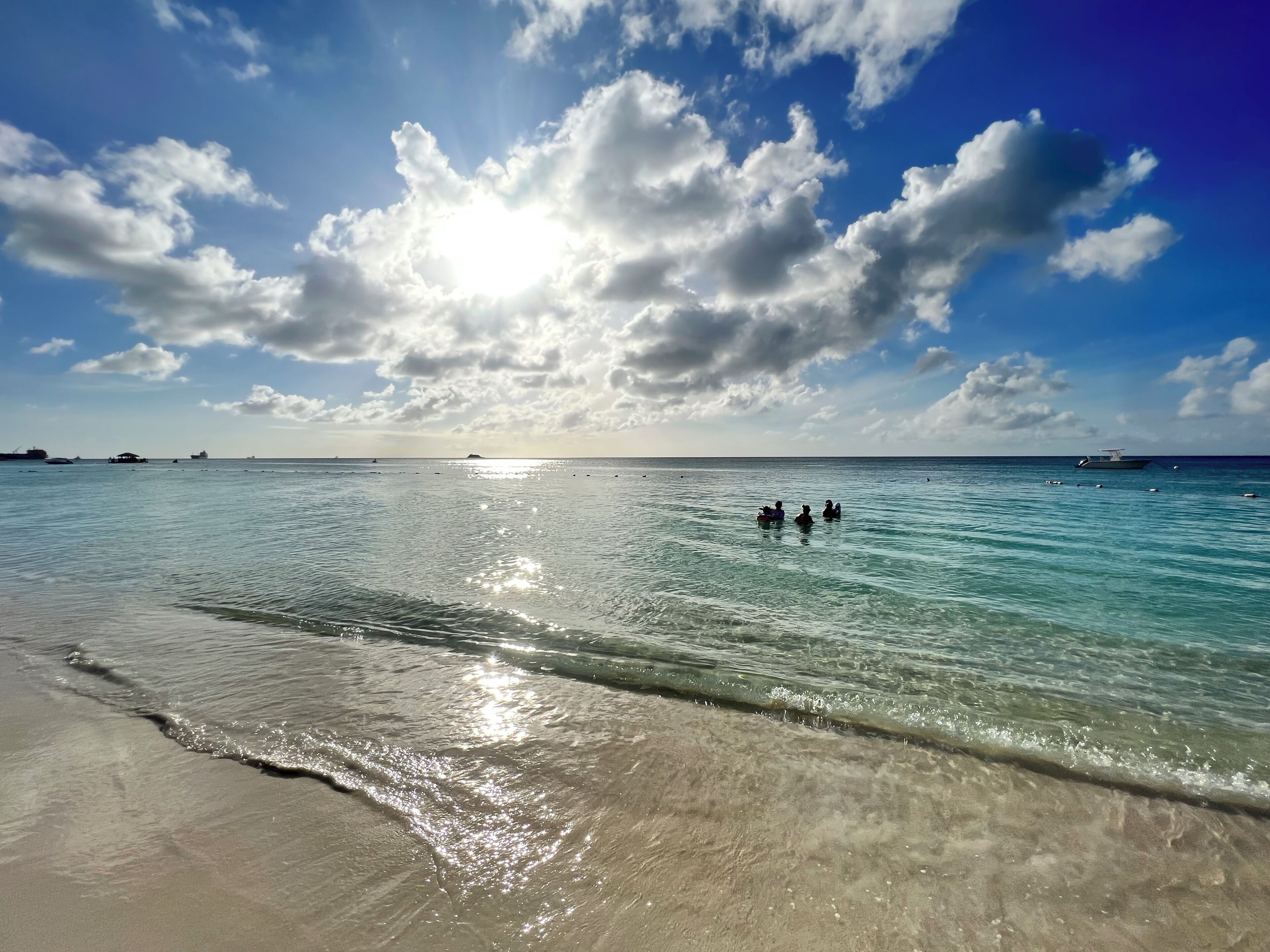 A beach with clear water, a sandy shore, and a partly cloudy sky.