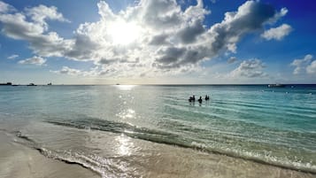 Una playa con aguas cristalinas, una orilla arenosa y un cielo parcialmente nublado.
