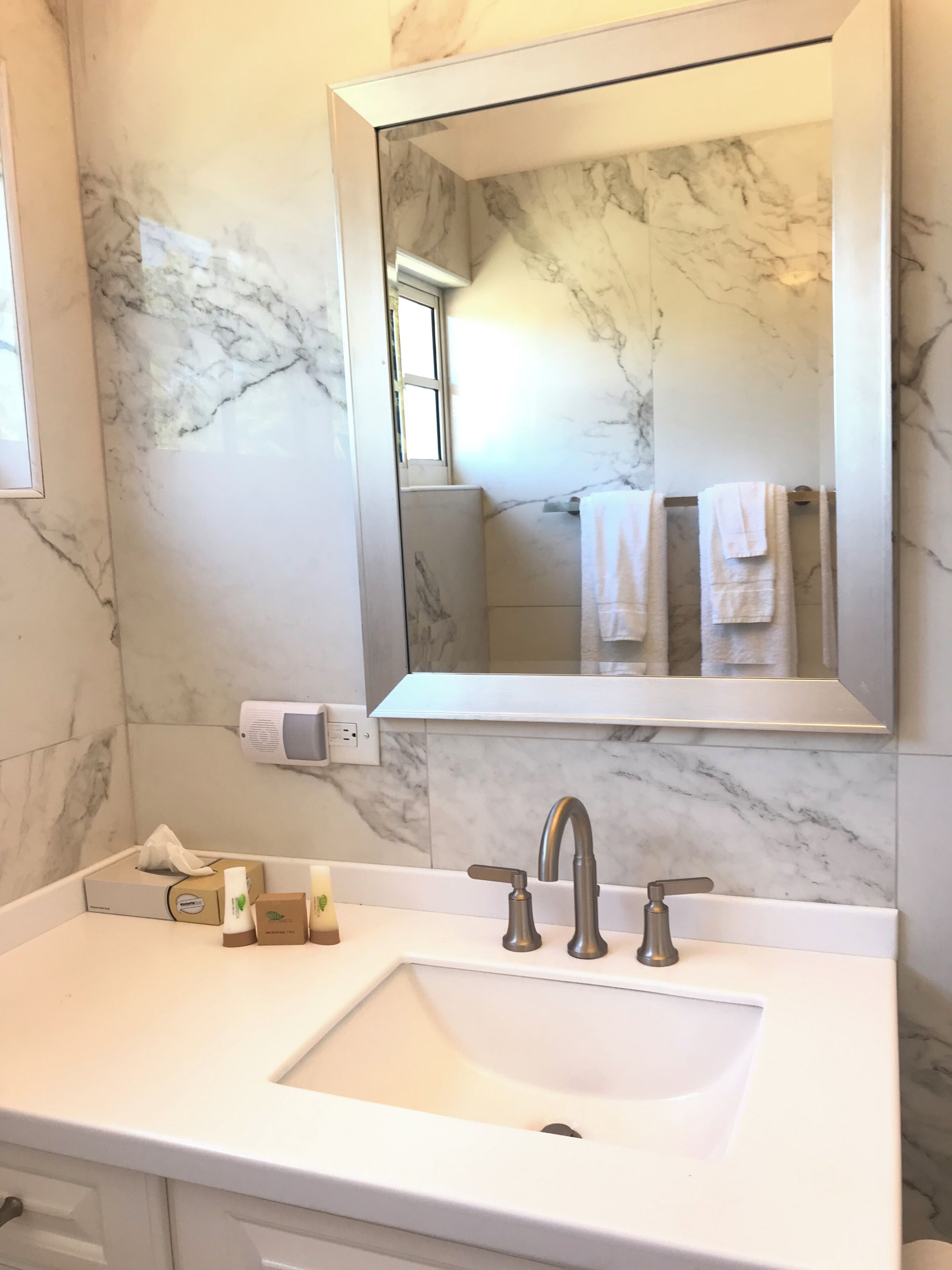 A bathroom with a marble wall, a large mirror, a sink with a modern faucet, and a towel rack with white towels.