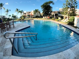 Una piscina de diseño curvo, rodeada de palmeras y sillas de descanso.