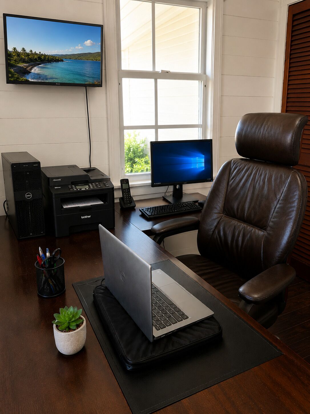 Un espacio de teletrabajo con escritorio, computadora, silla, impresora y televisor en la pared.