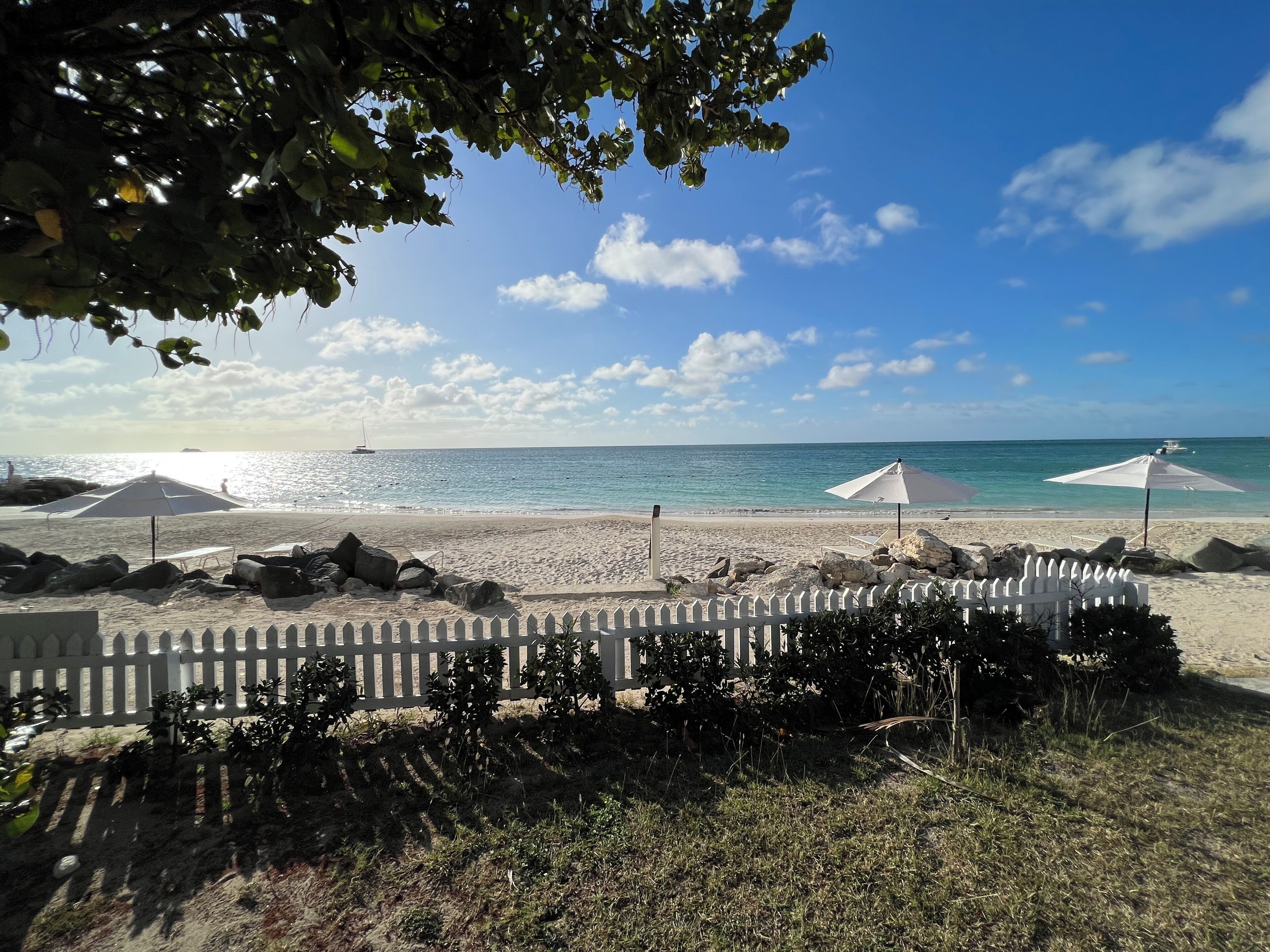A beach with umbrellas, a white picket fence, and a clear sky.