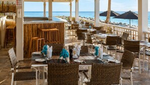 A beachside restaurant with wicker furniture, hanging wicker lamps, and a view of the sea.