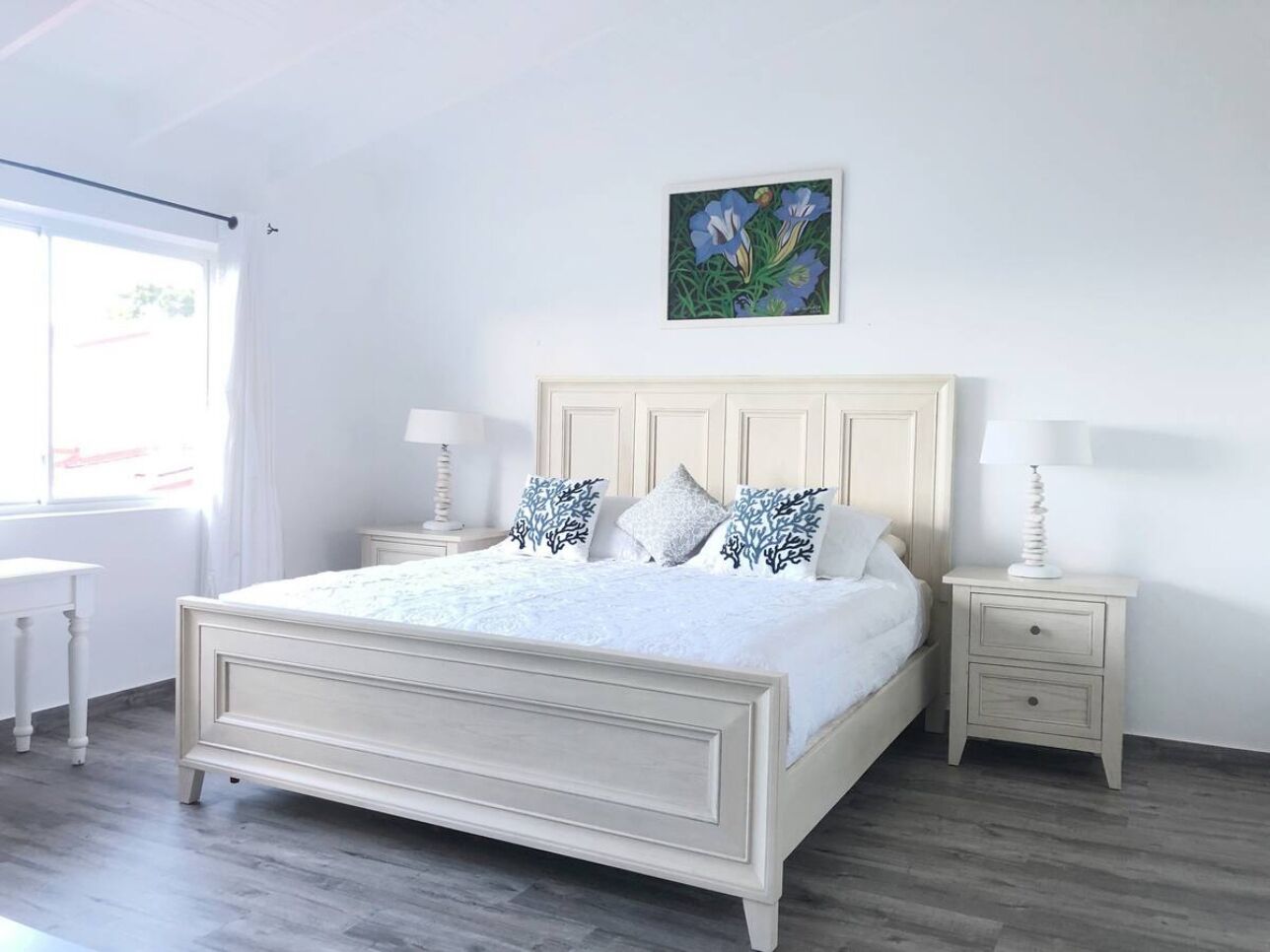 Ein Schlafzimmer mit einem großen Bett, zwei Nachttischen, einem Fenster mit Vorhängen und einem Gemälde an der Wand.