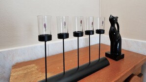 Una repisa de madera con cinco candelabros de vidrio y una figurita de gato negro.