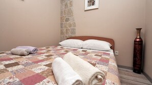 Una cama bien hecha con colcha estampada y toallas enrolladas, una pared de piedra y un jarrón en el suelo.