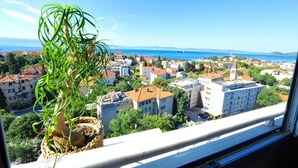 Un balcón con planta en maceta, con vistas a un pueblo costero con edificios y un cielo azul despejado.