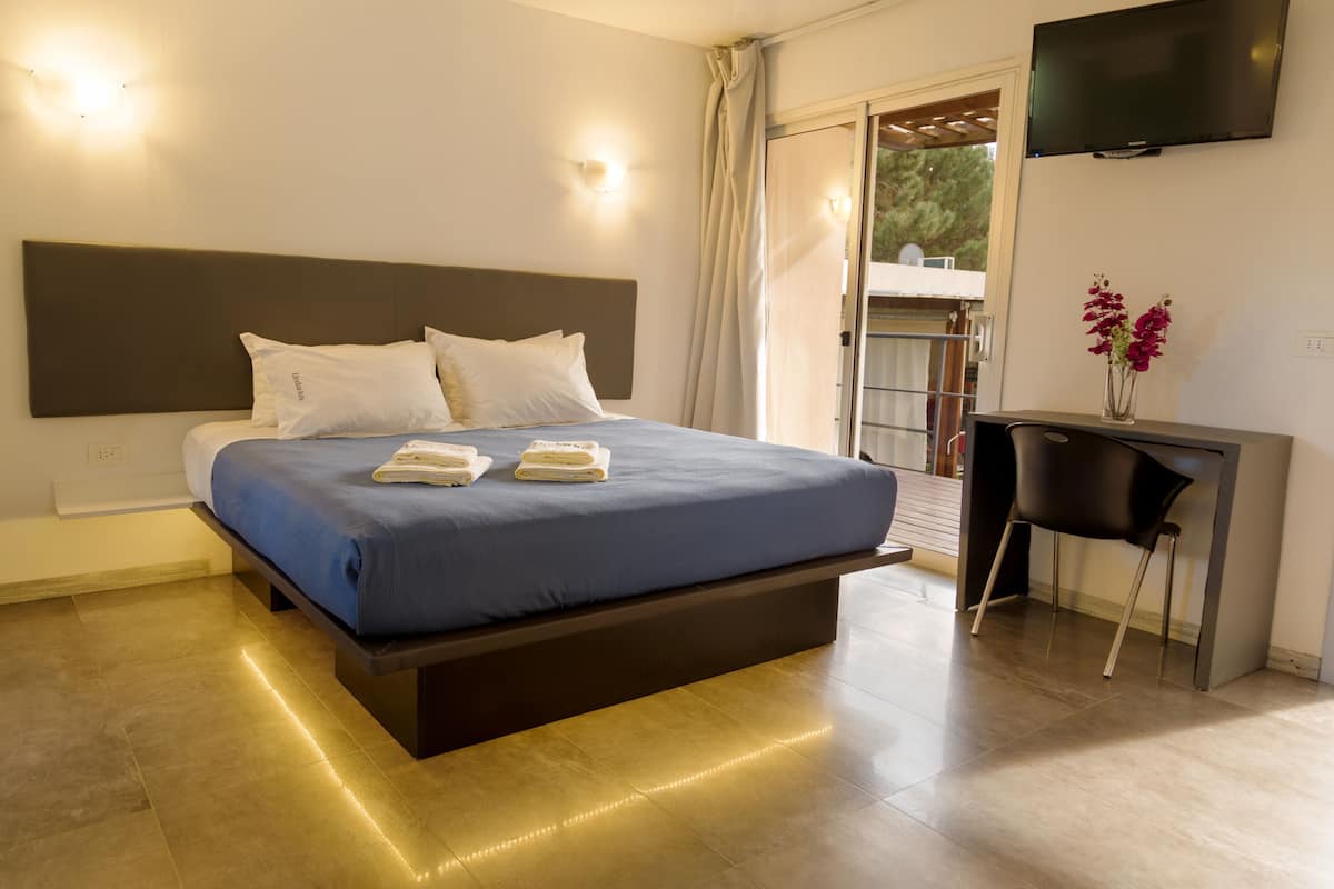 A modern hotel room with a large bed, a desk, and a TV on the wall.