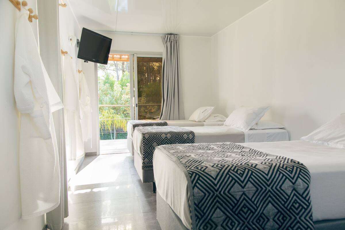 A hotel room with two beds, a TV, and a balcony with a view of greenery.
