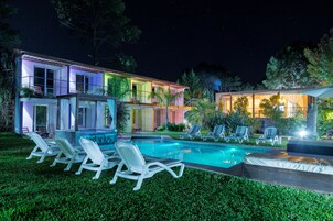 A modern house with a swimming pool, lounge chairs, and a well-lit outdoor area at night.