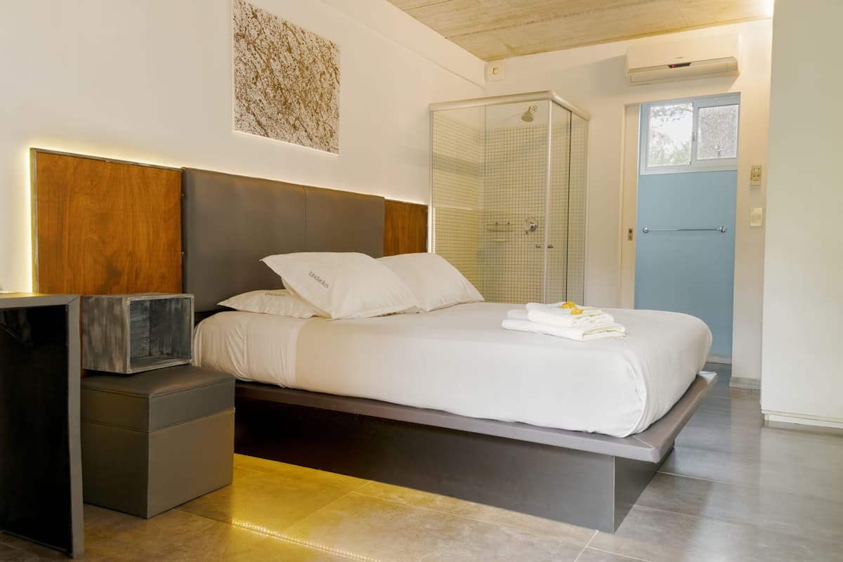 A modern bedroom with a bed, bedside table, and a shower area.