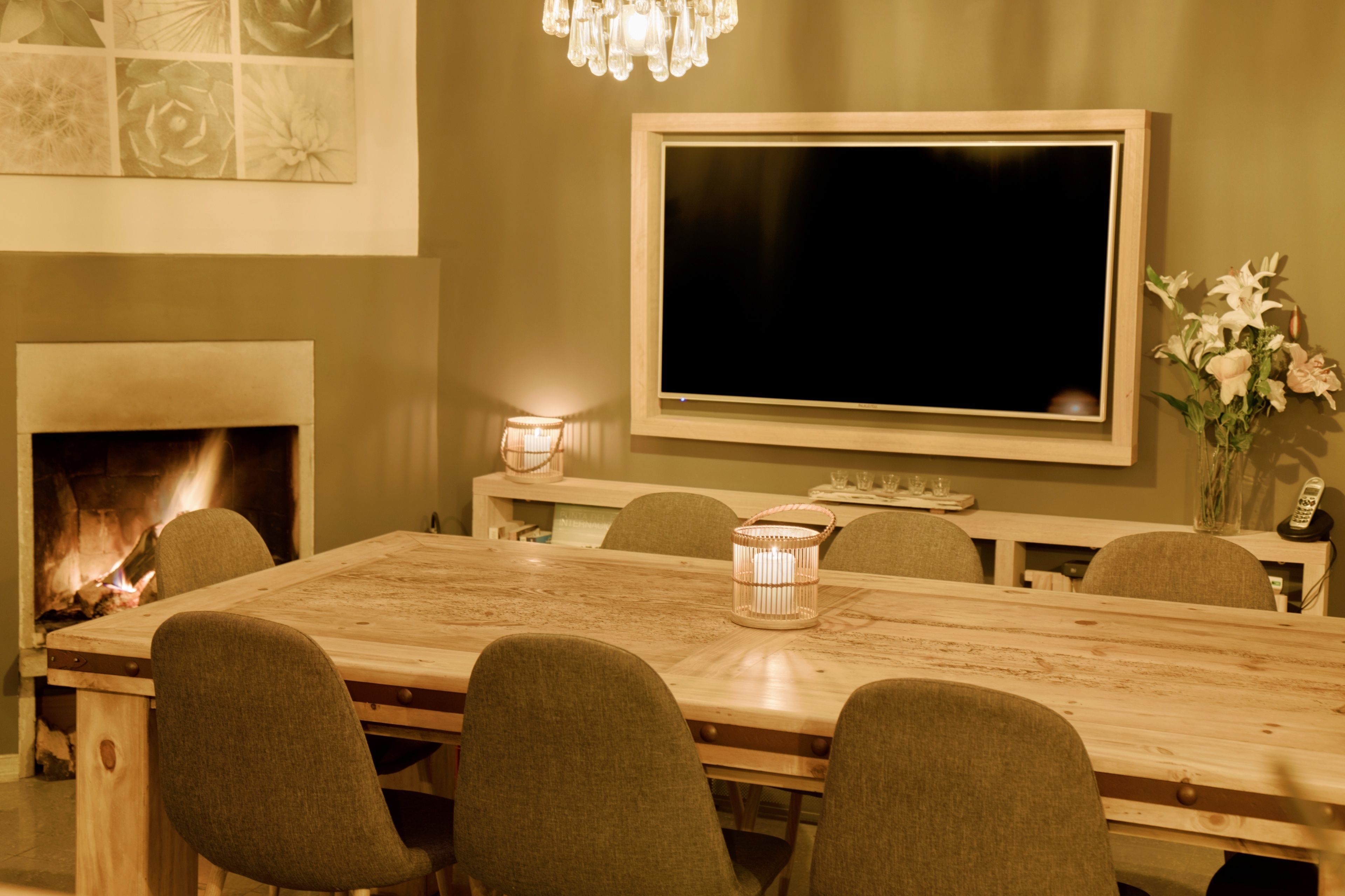 Un coin repas avec une table en bois, six chaises, une cheminée, un téléviseur à écran plat fixé au mur et un vase avec des fleurs sur la table.
