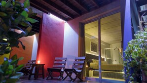A wooden deck with three wooden chairs and a small table, a sliding glass door leading to a room, and a plant in the foreground. - Undarius Hotel - Clothing Optional Hotel Exclusively for Gay Men (Chihuahua)