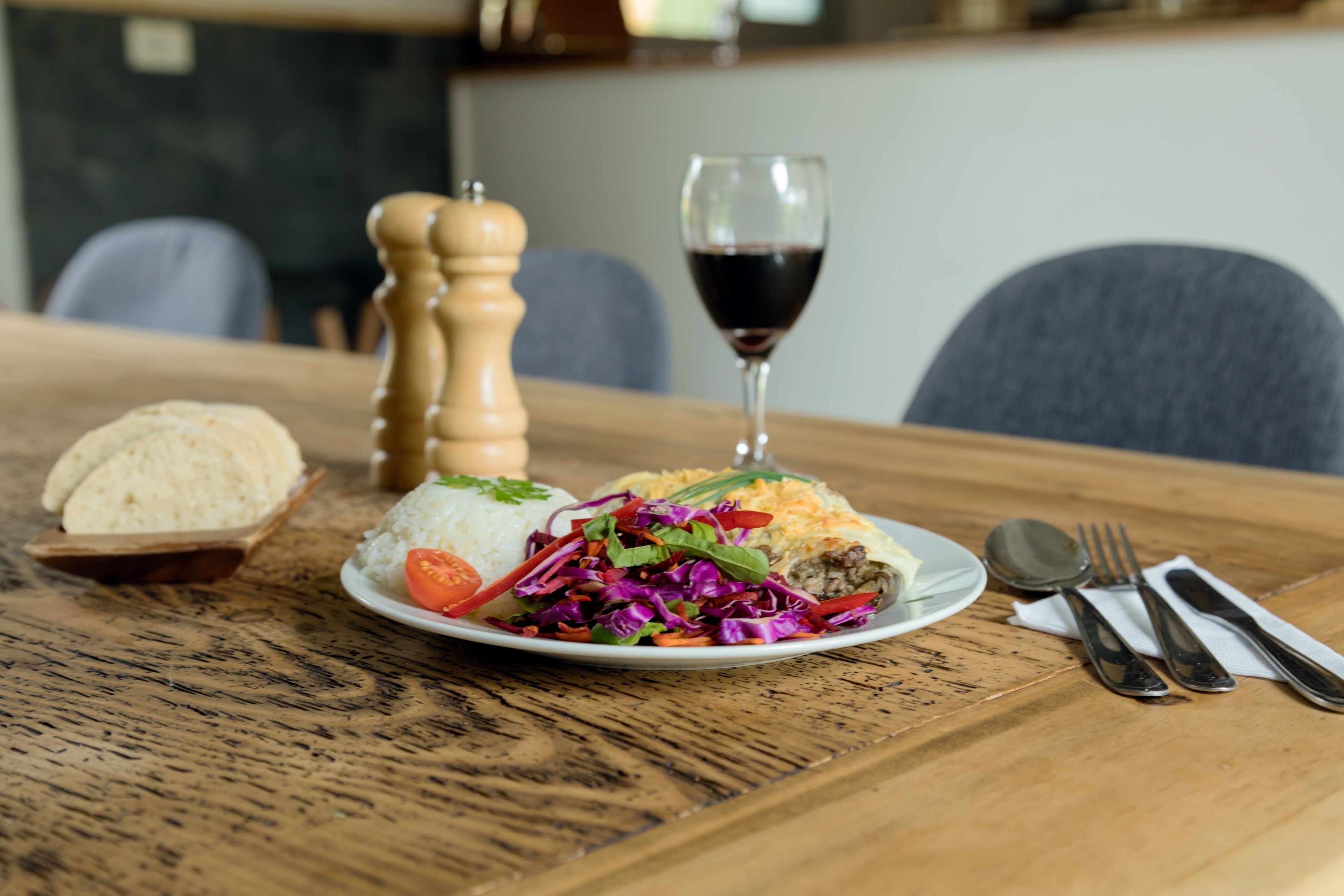 Uma mesa de madeira com um prato de comida, um copo de vinho tinto e talheres.