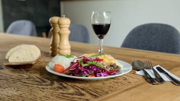 Uma mesa de madeira com um prato de comida, um copo de vinho tinto e talheres.
