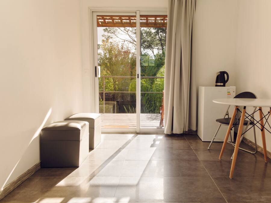 Una camera moderna con una porta scorrevole in vetro che dà su un balcone, un piccolo tavolo rotondo con una sedia e una panca.