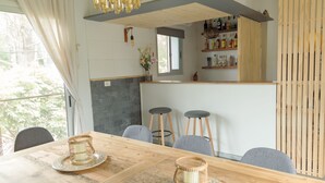 A dining area with a wooden table, two bar stools, and a kitchen counter with shelves. - Undarius Hotel - Clothing Optional Hotel Exclusively for Gay Men (Chihuahua)