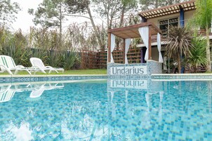 A swimming pool with lounge chairs, a pergola with a canopy, and a building labeled "Undaria."